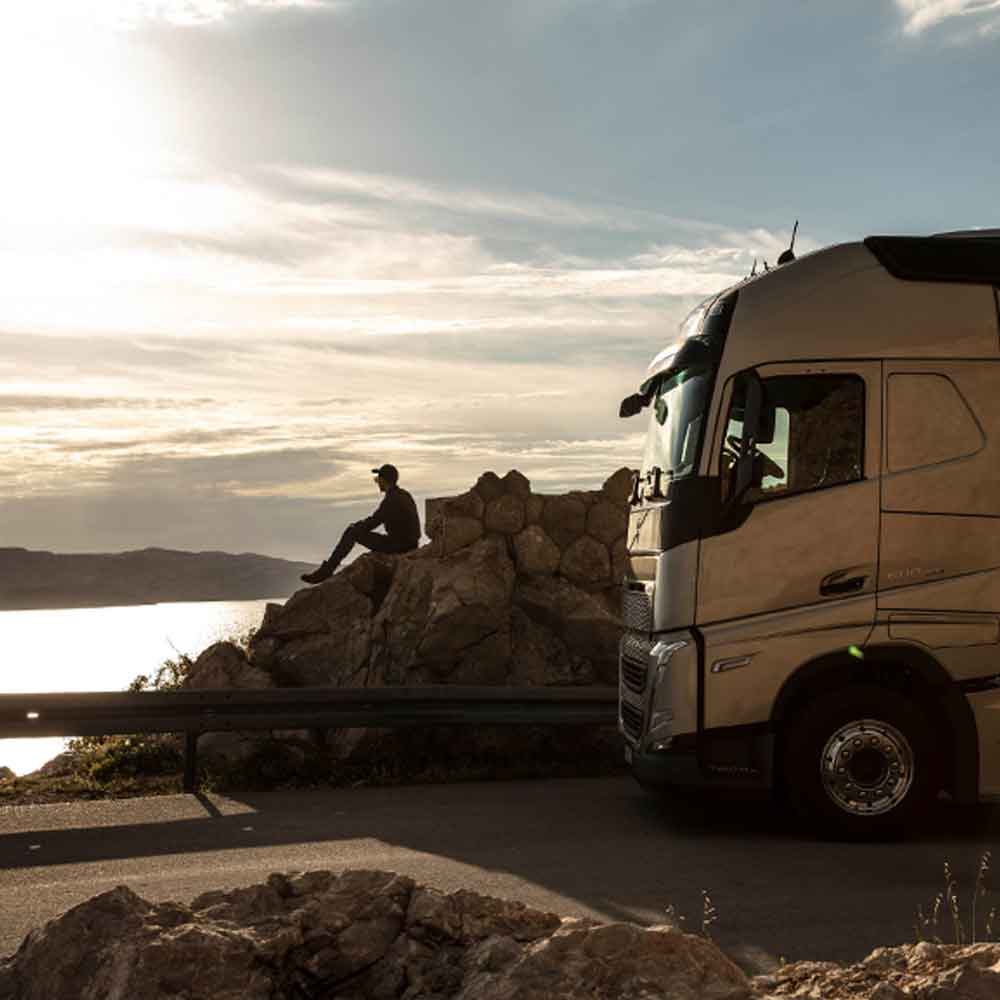 Kierowca siedzi na skale o zachodzie słońca obok zaparkowanego Volvo FH